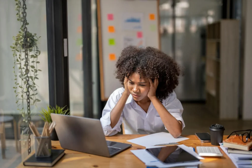 Young professional experiencing burnout while working at a desk, illustrating the pressures of hustle culture.